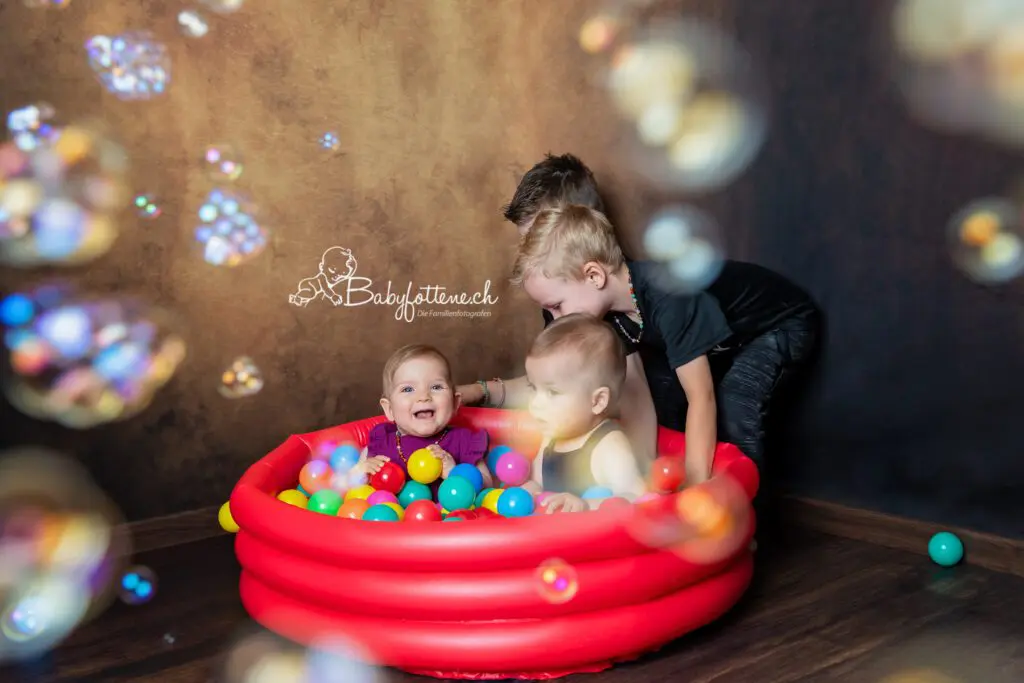 Babyfotografie Zürcher Oberland - Zwillinge im Bällebad beim Fotoshooting und ihre grossen Brüder helfen ihnen